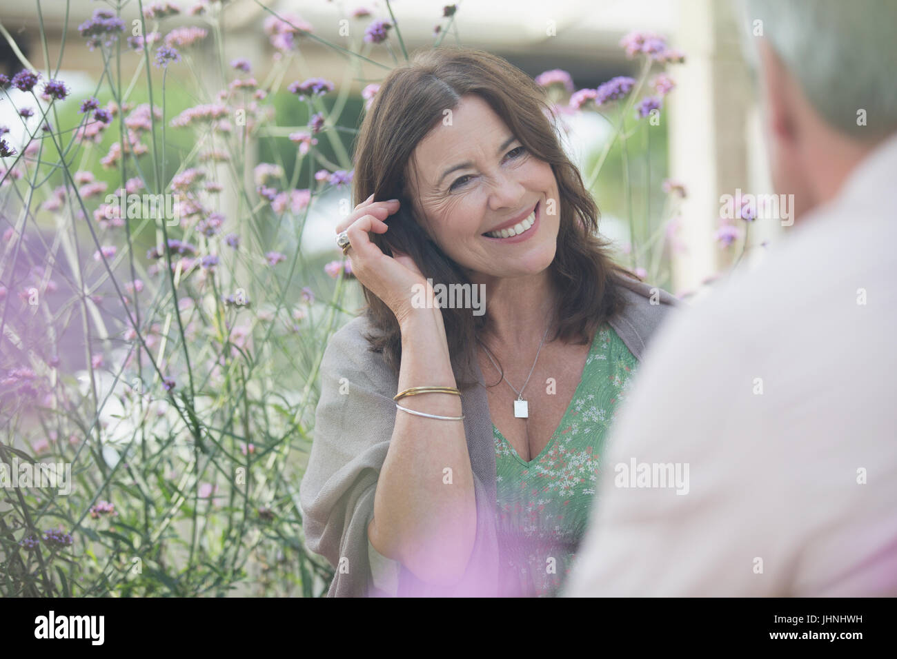 Smiling mature woman talking to man on patio with purple flowers Stock Photo