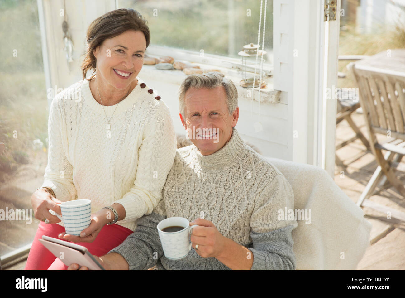 Portrait smiling mature couple using digital tablet and drinking coffee on sun porch Stock Photo