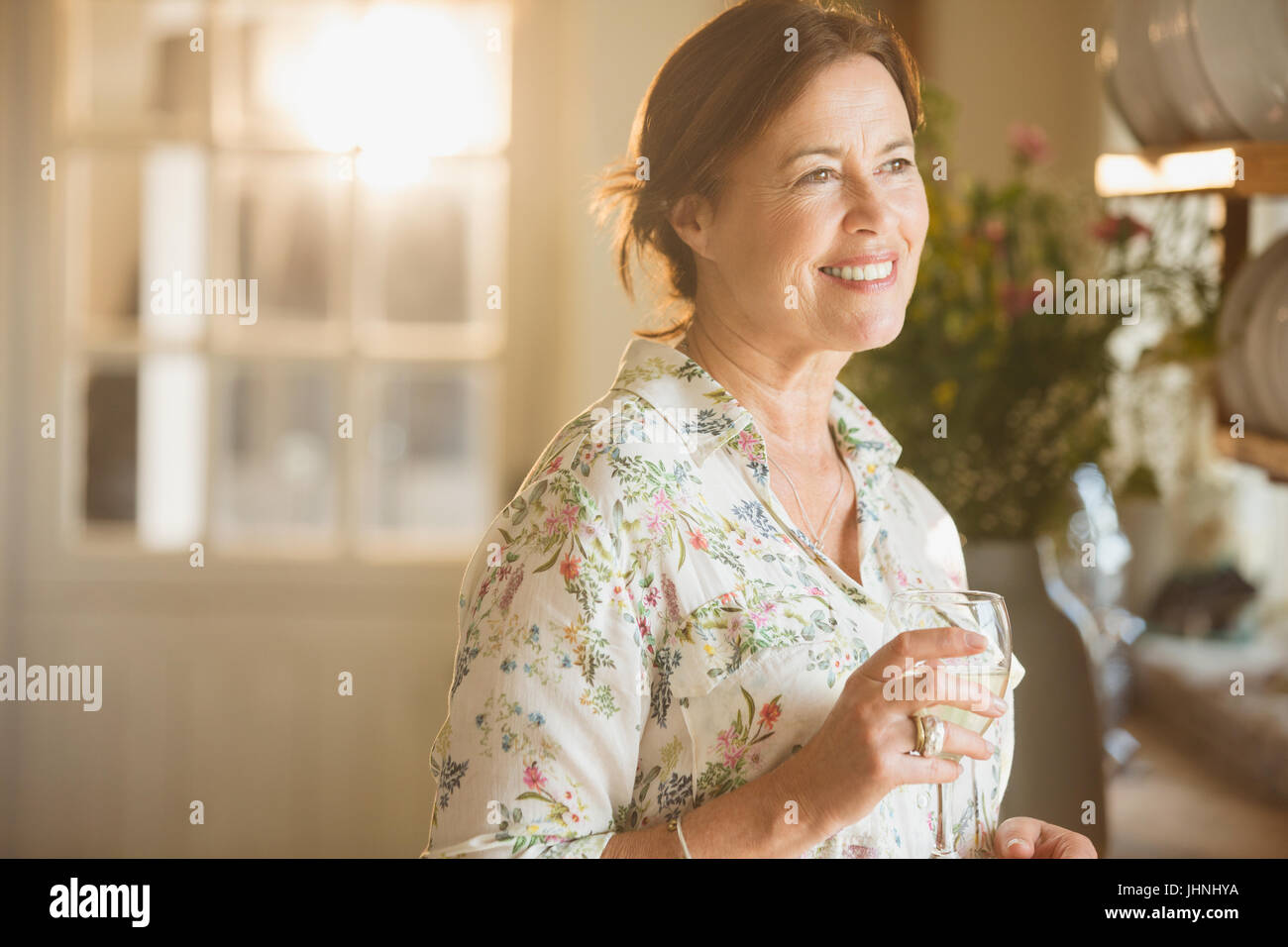 Smiling mature woman drinking wine in kitchen Stock Photo