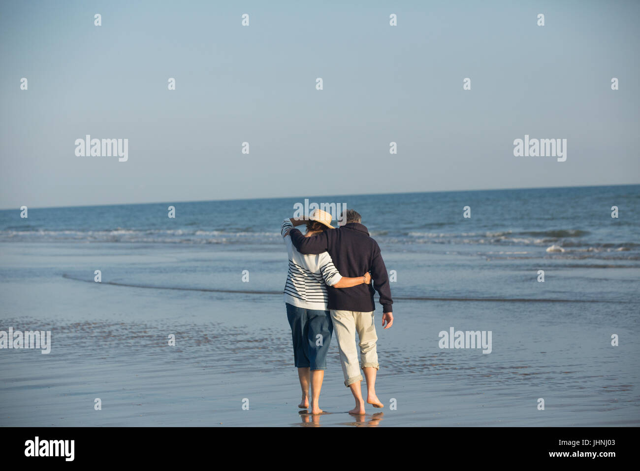 Affectionate mature couple hugging, walking in sunny ocean beach surf Stock Photo