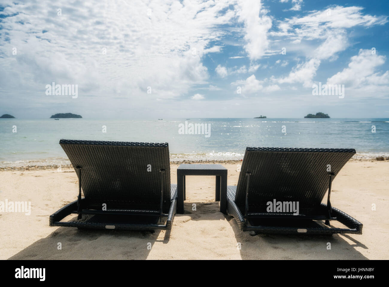Beach chairs on the sandy beaches for tourists to sit and relax with soft ocean waves breaking on beach. Summer travel vacation and holiday concept. Stock Photo