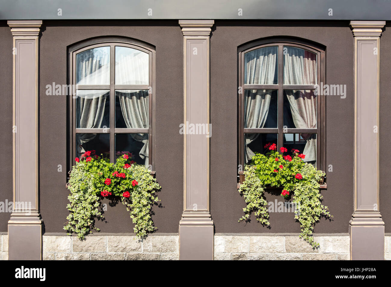old house with windows decorated with geranium flowers and ivy in flower boxes Stock Photo