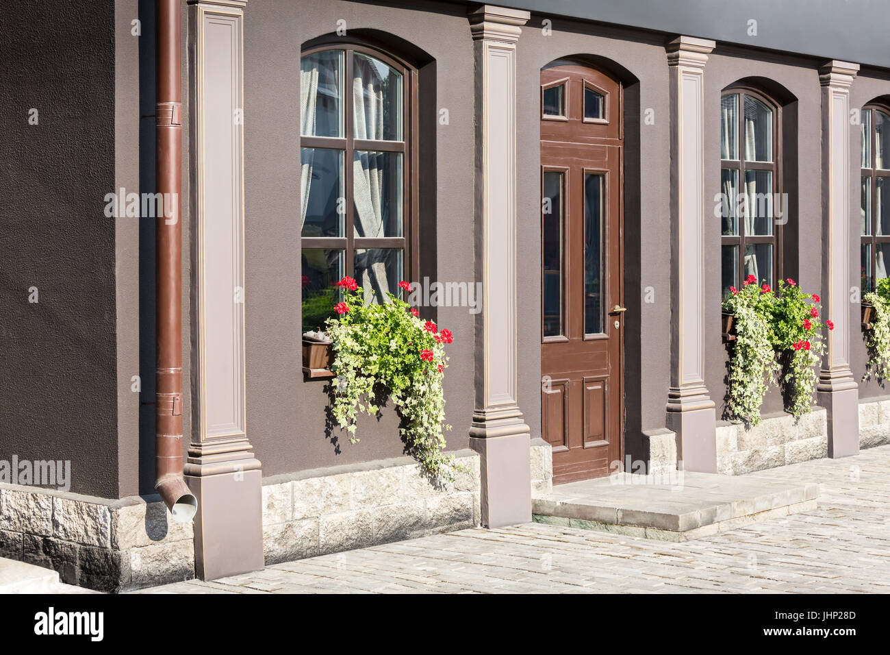 old house facade with windows decorated with ivy and geranium flowers in flowerpots Stock Photo