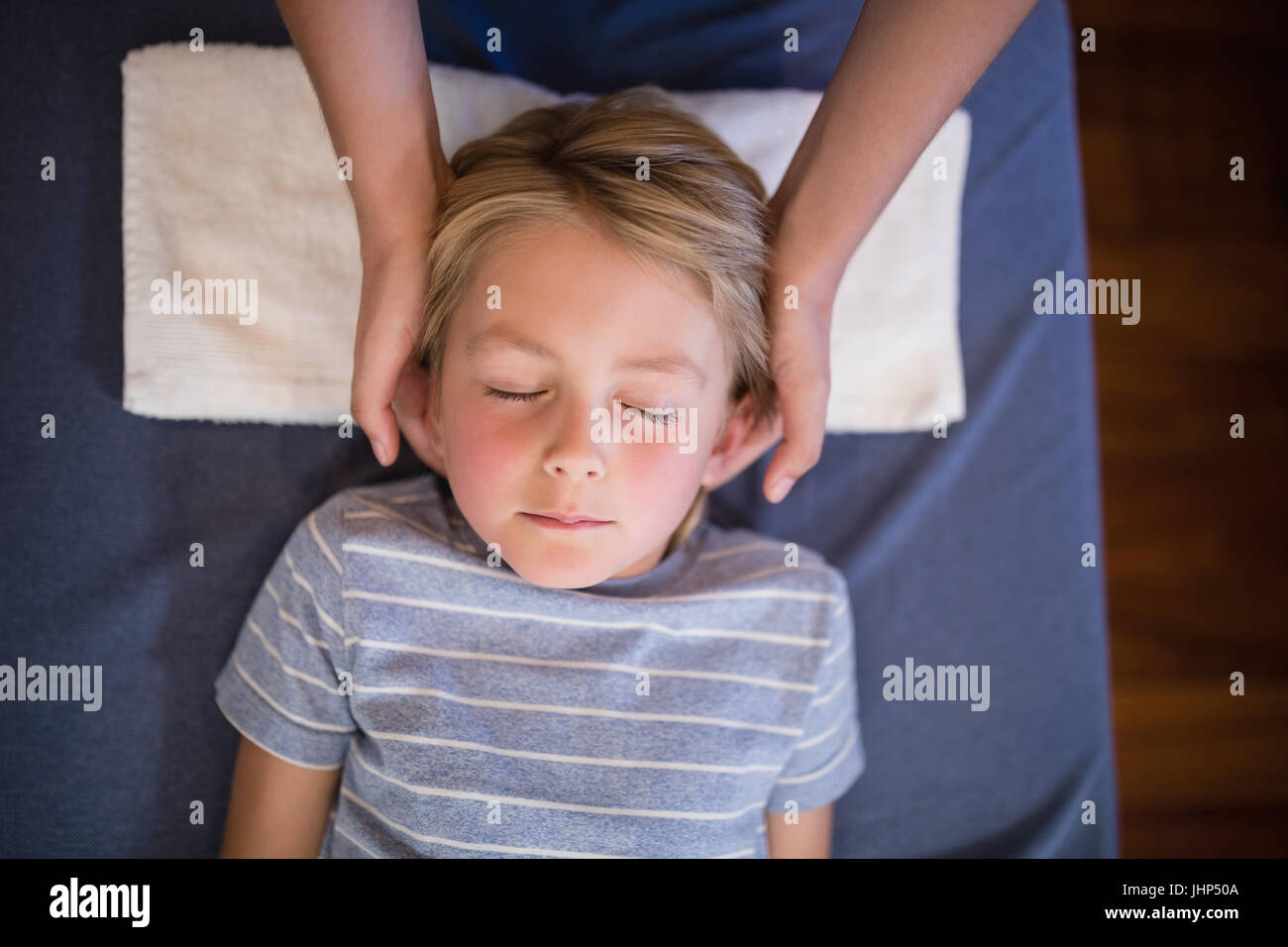 Overhead view of boy with eyes closed receiving neck massage from female therapist at hospital ward Stock Photo