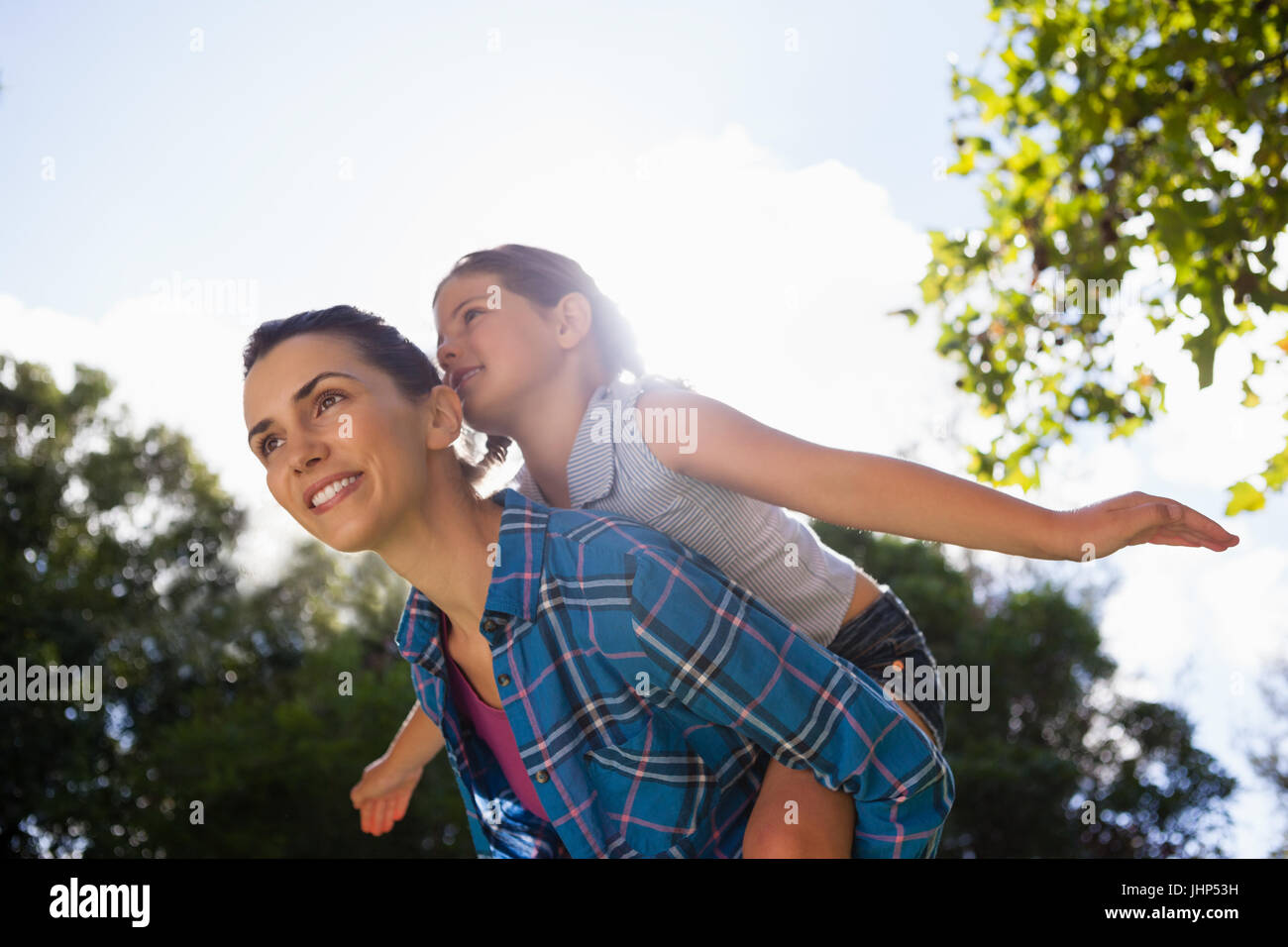 Low angle view of girl with arms outstretched enjoying piggyback ride on mother against sky in backyard Stock Photo