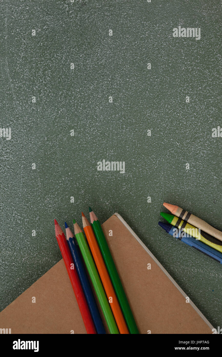 Close-up of color pencil, crayons and book on chalkboard Stock Photo