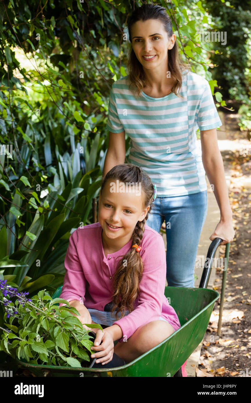 Happy mother pushing girl with flowers sitting in wheelbarrow at ...