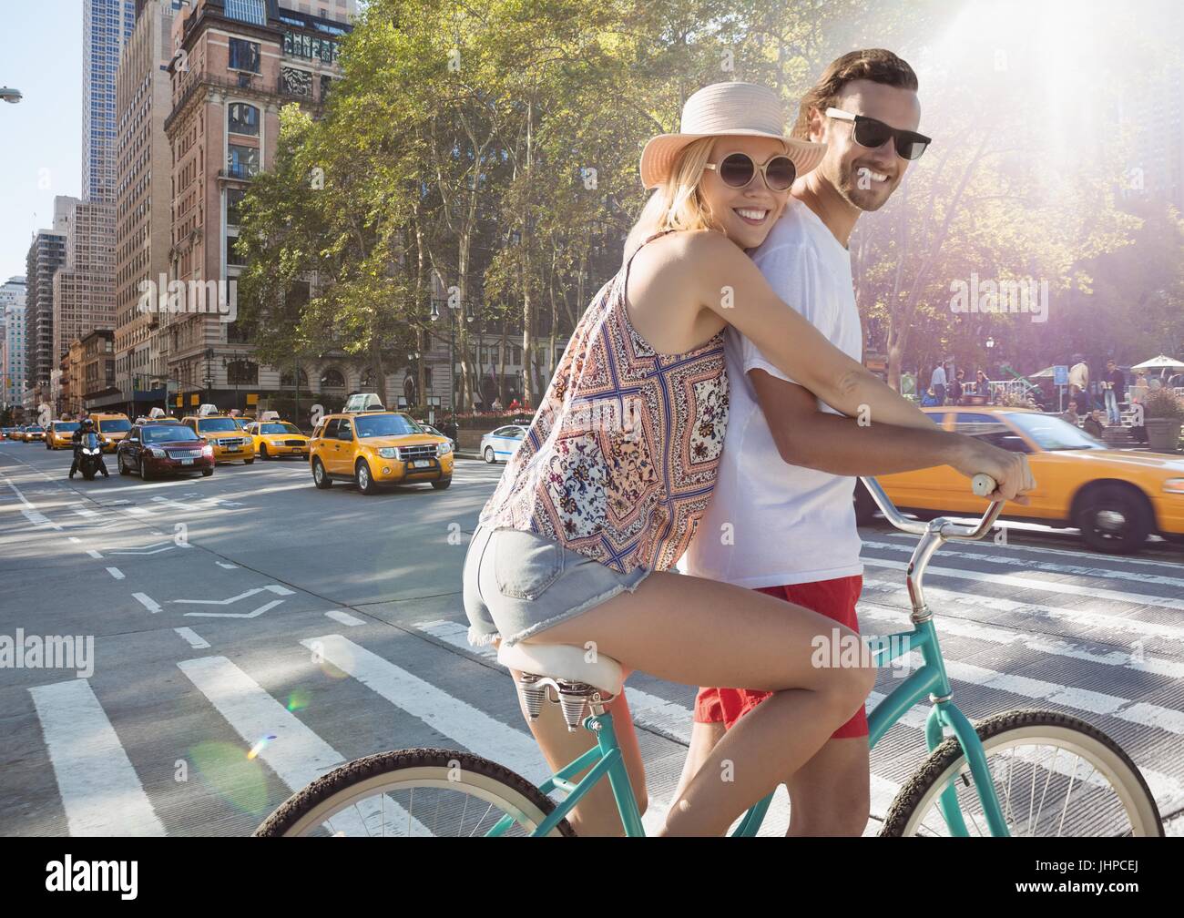 Digital composite of Millennial couple on bike against street with flare Stock Photo