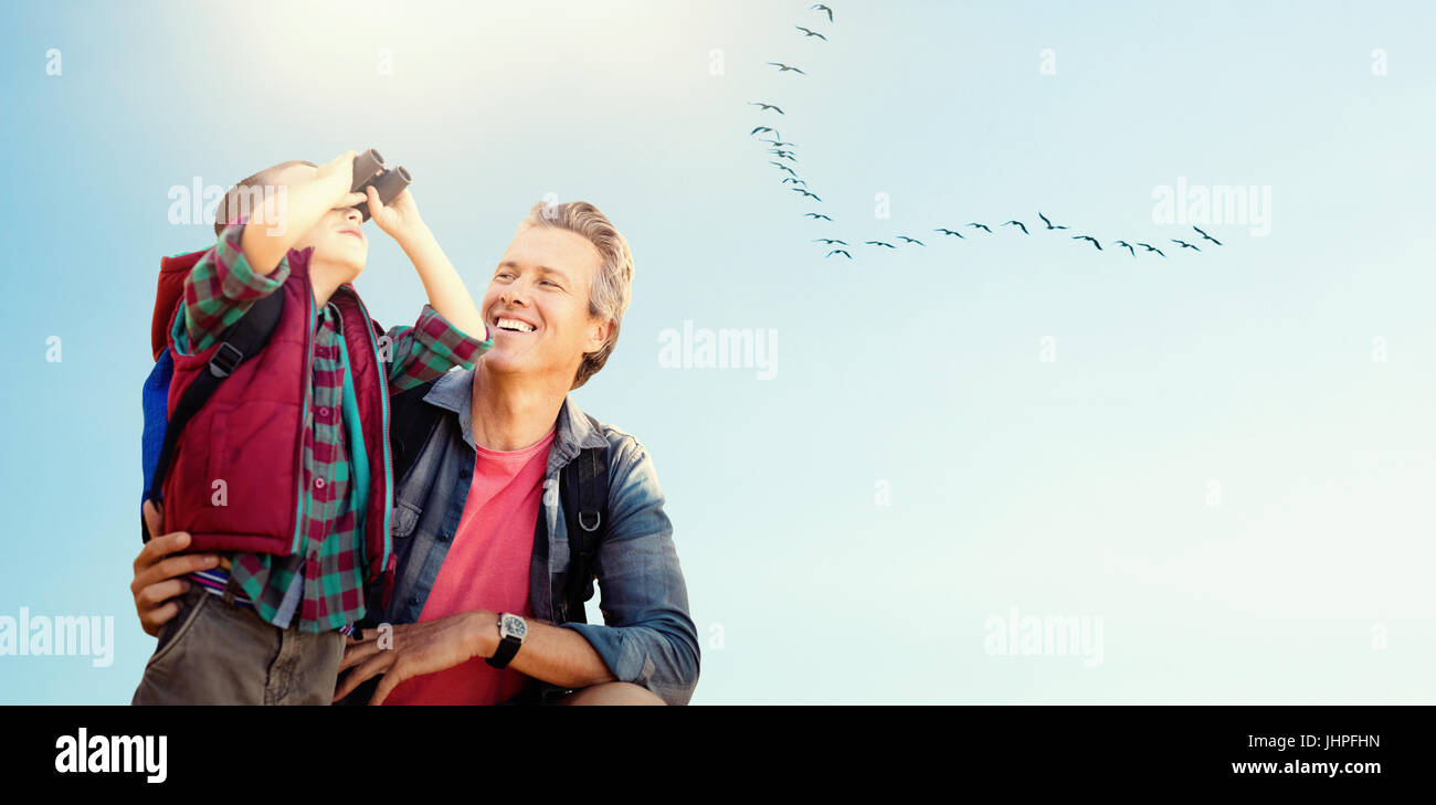 Little boy using binocular with his father against flock of bird flying