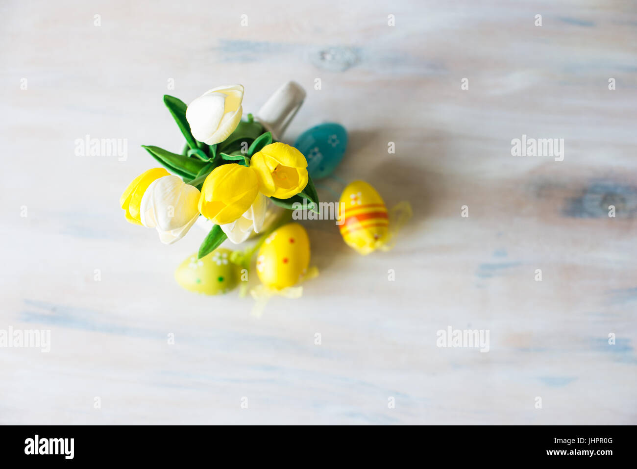 Bright yellow and white tulips in a vase with colorful easter eggs on ...