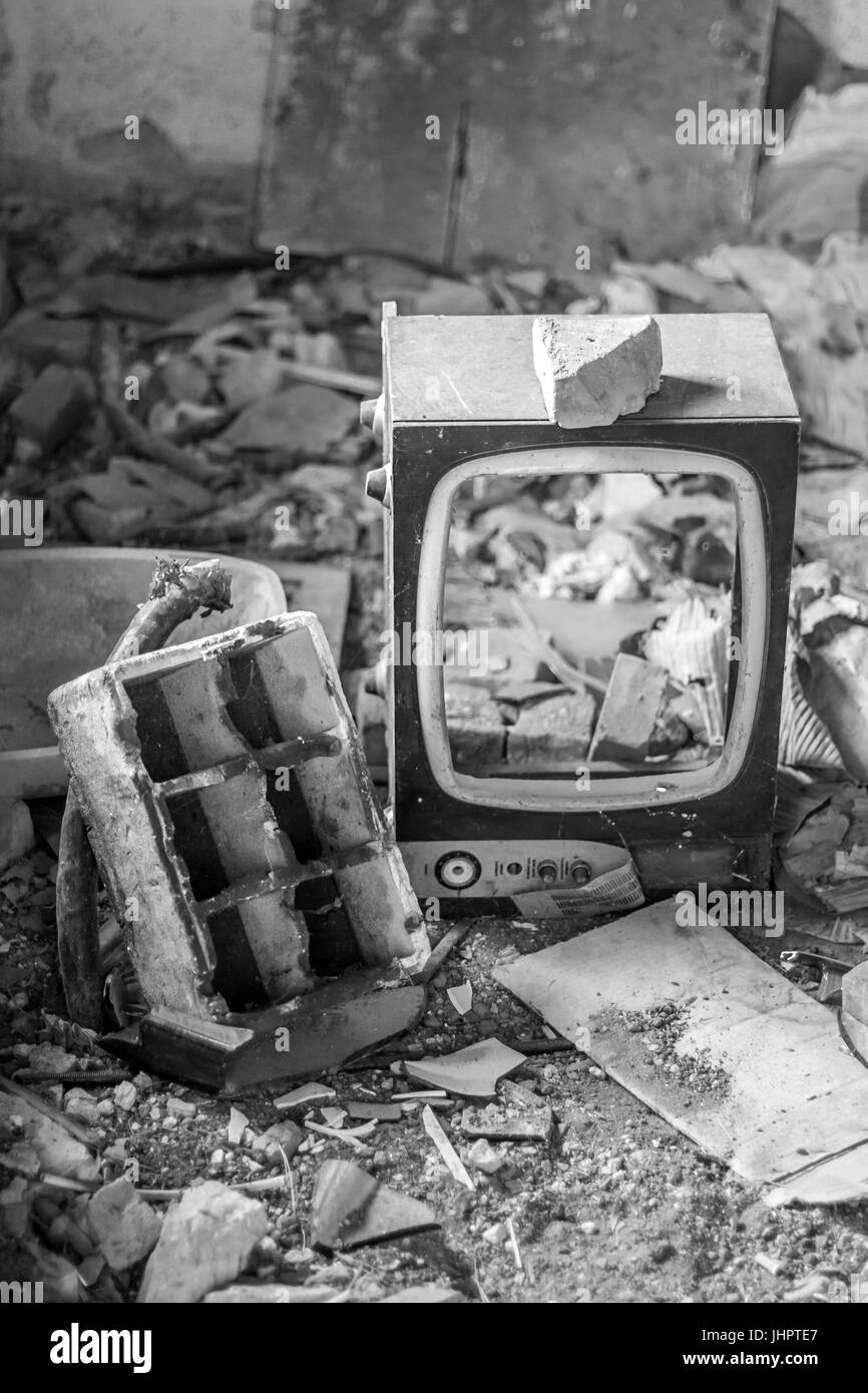Broken CRT Television Set in abandoned room with many pieces of broken objects and dirt, in black and white Stock Photo