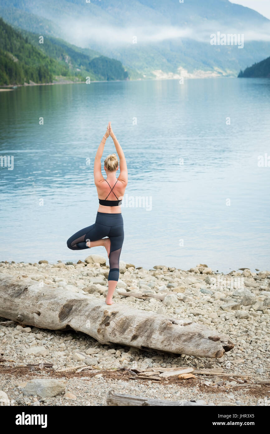 Rear view of woman practicing tree pose on log at lakeshore Stock Photo ...