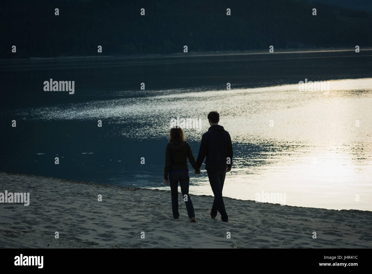Silhouette of couple walking with hand in hand near lake Stock Photo ...