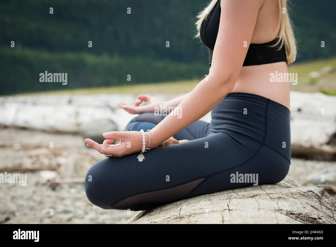 Low section of woman practicing lotus position on log at lakeshore Stock Photo