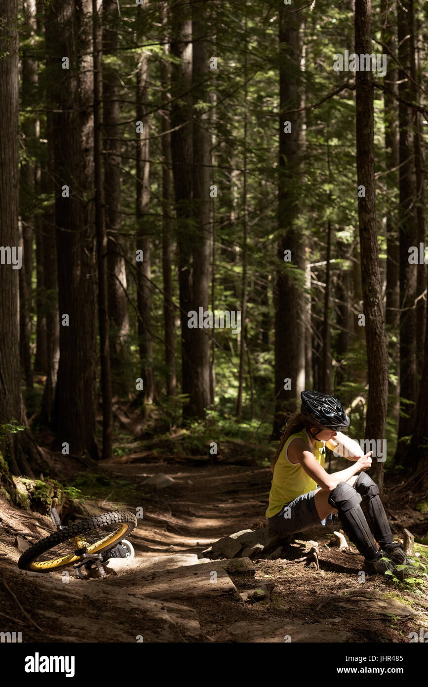 Woman sitting on rock by unicycle against trees in forest Stock Photo