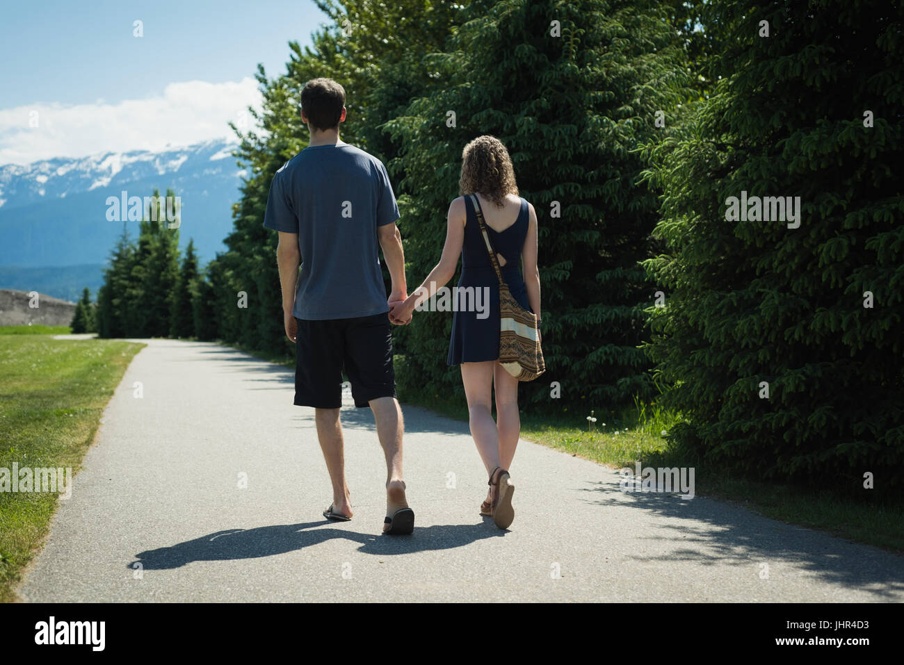 Rear view of couple holding hands and walking on countryside road on a ...