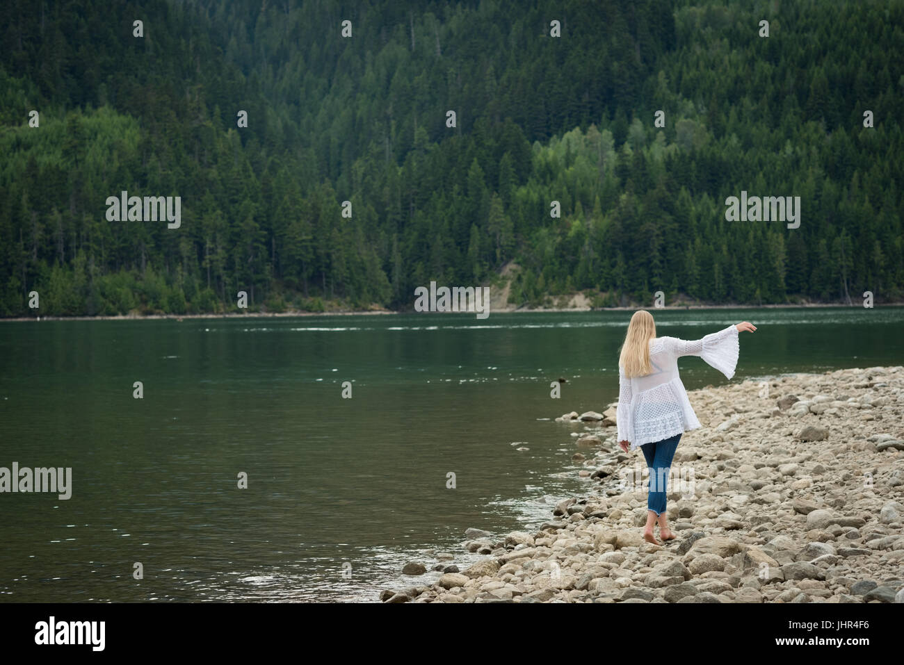 Rear view of young woman walking at lakeshore against trees Stock Photo ...