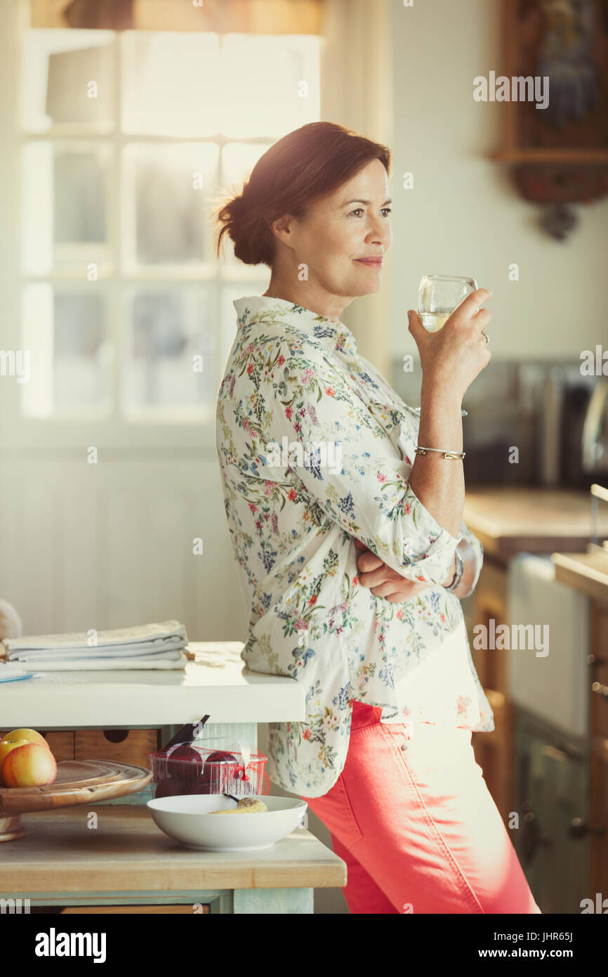 Pensive mature woman drinking wine in kitchen Stock Photo