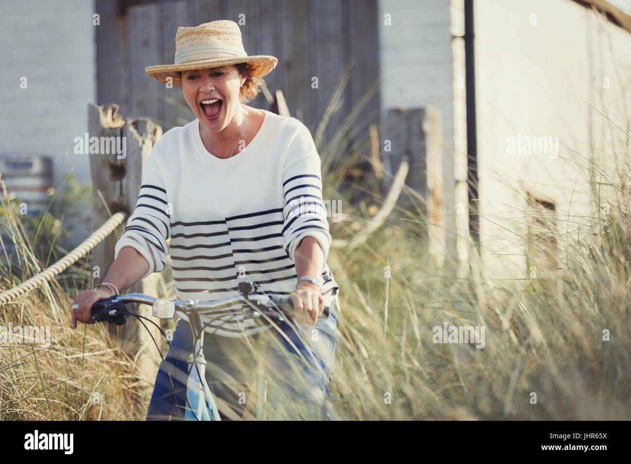Playful mature woman riding bicycle on beach grass path Stock Photo