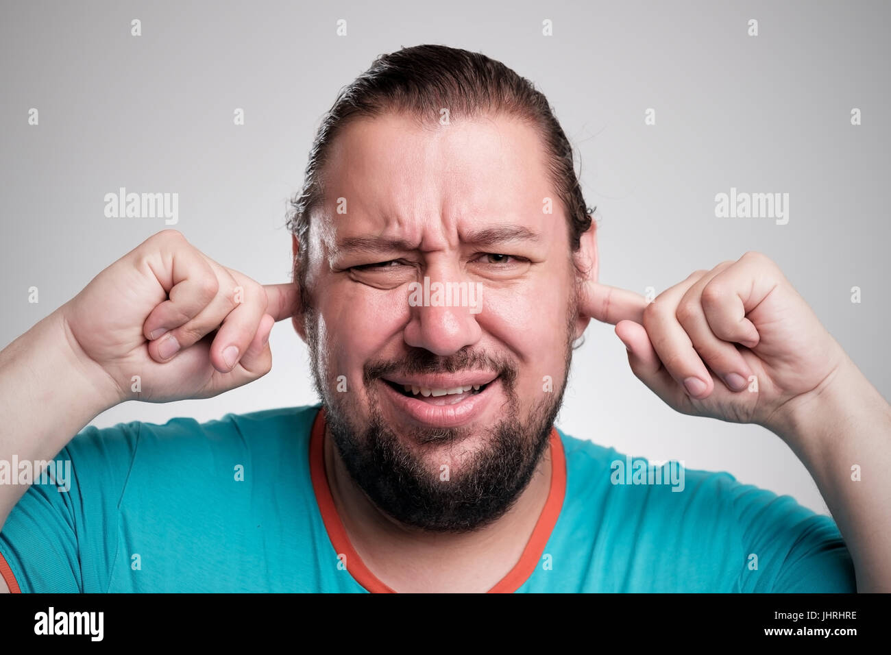 Can't hear it anymore. Portrait of young men closing his ears by hands isolated on grey. Stock Photo