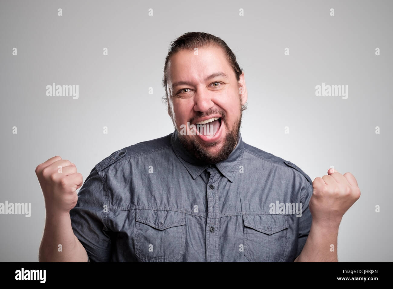 I won Happy young man gesturing and smiling while standing against gray background Stock Photo