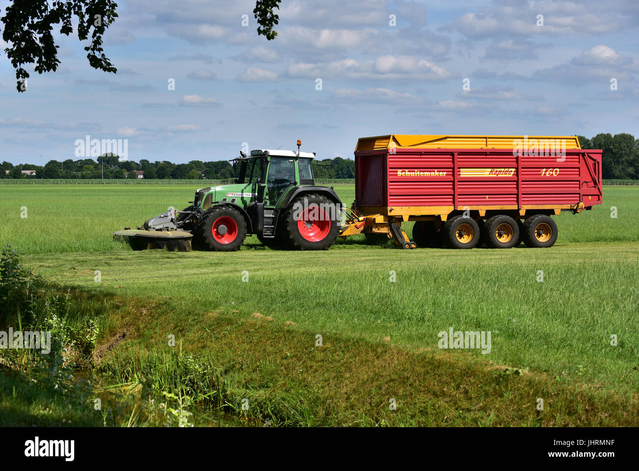 Tractor mowing with Ffront-mounted disc mowers and pulling a self-loading Schuitemaker Forage wagon Stock Photo