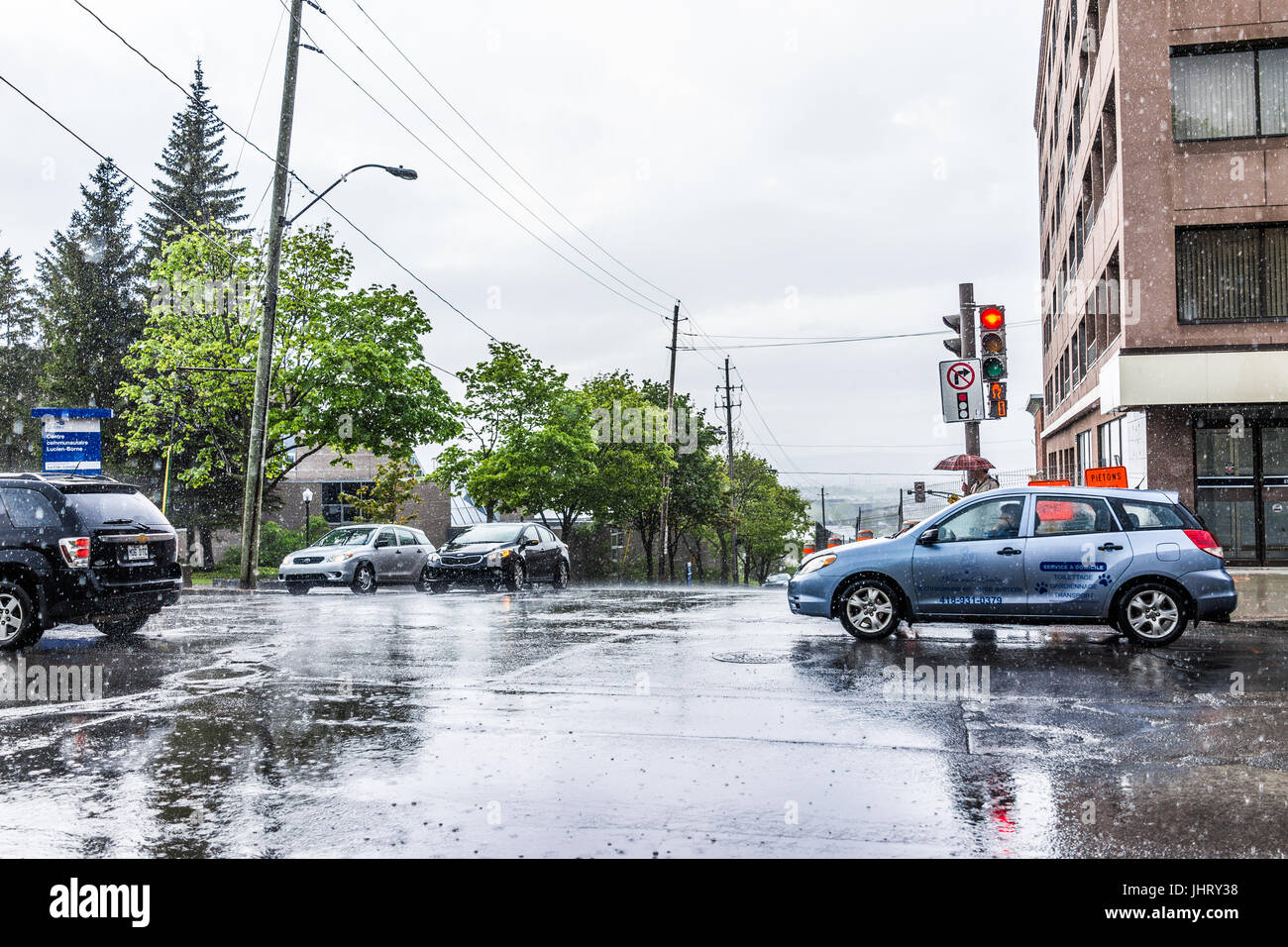 Quebec City, Canada - May 30, 2017: Saint Jean Baptiste Limoilou area with traffic intersection, cars, heavy rain, puddles and people Stock Photo