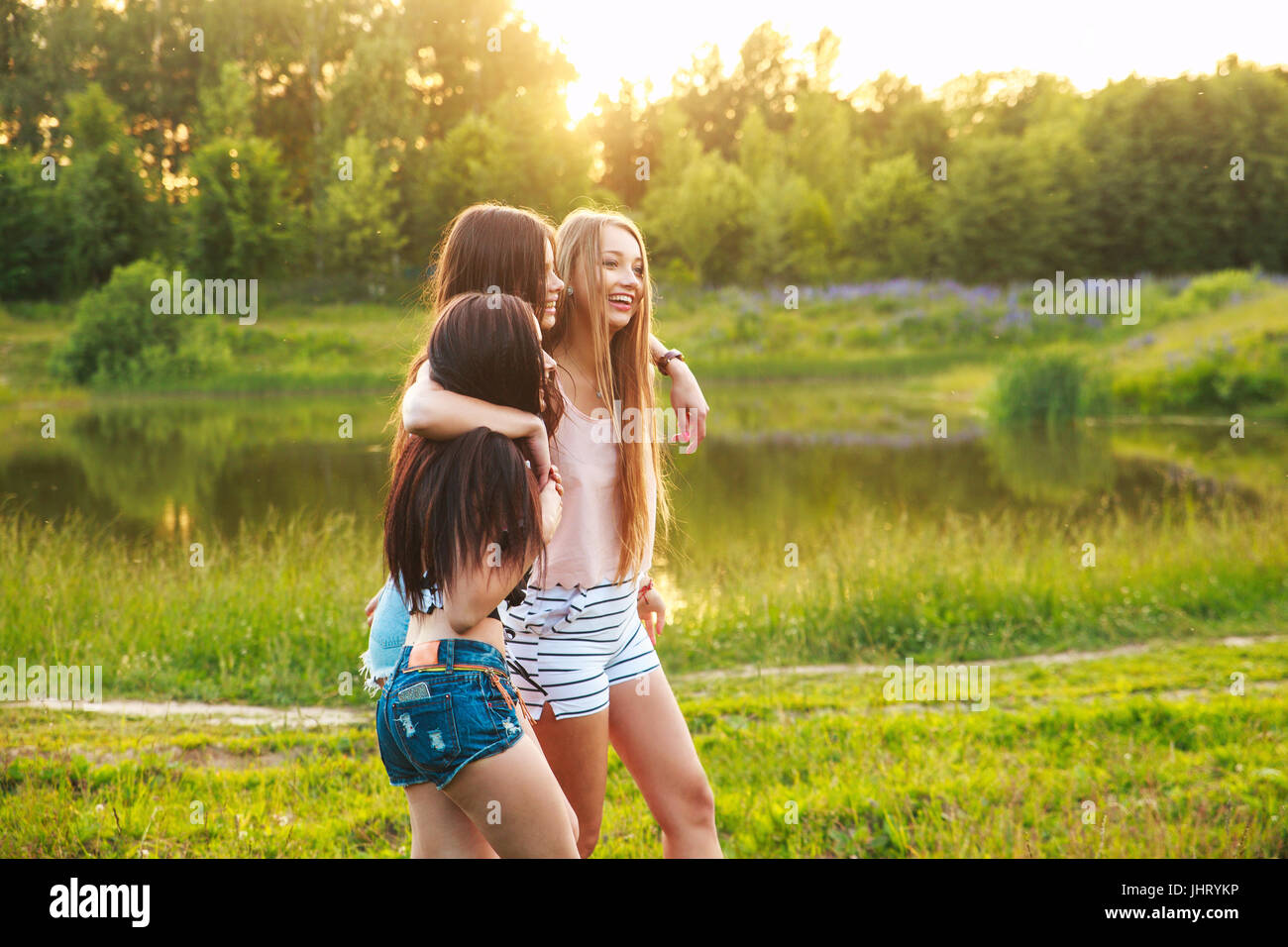 three beautiful girls walking and laughing on sunset in the park. Friendship concept. Stock Photo