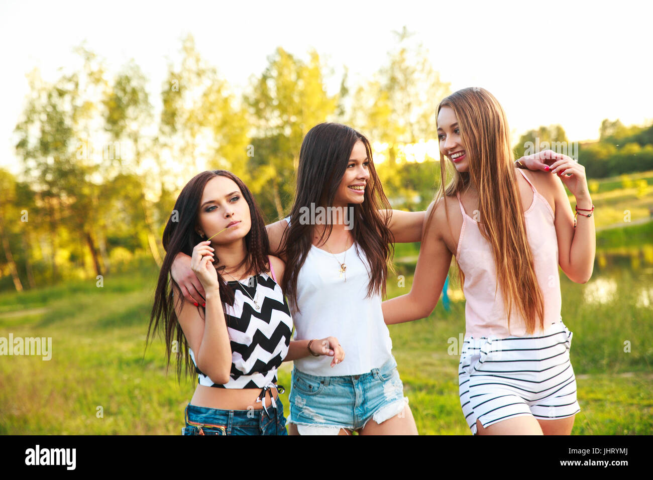 three beautiful girls walking and laughing on sunset in the park. Friendship concept. Stock Photo