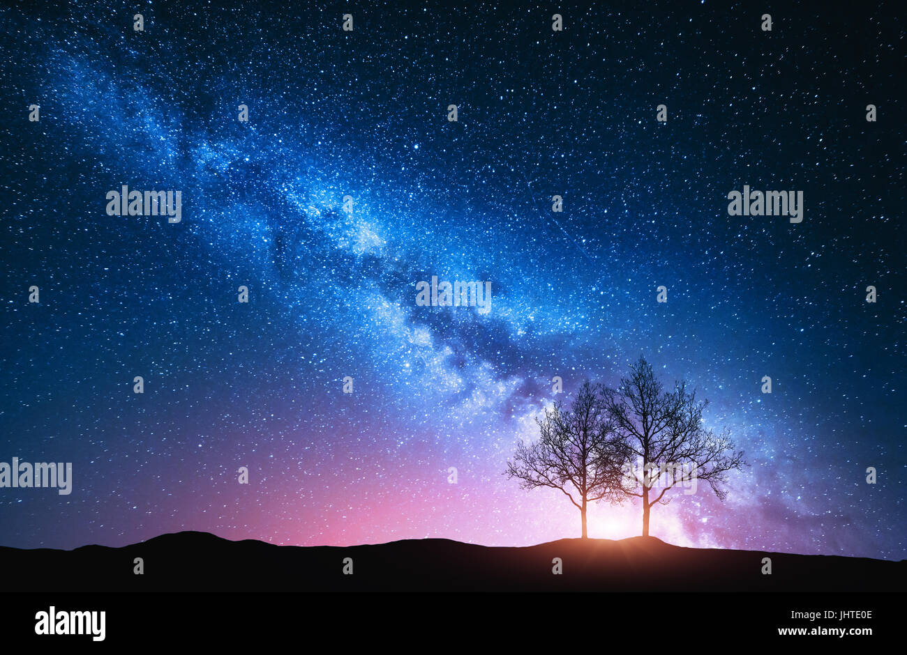 Starry sky with pink Milky Way and trees. Night landscape with alone trees on the hill against colorful milky way. Amazing galaxy. Nature background w Stock Photo