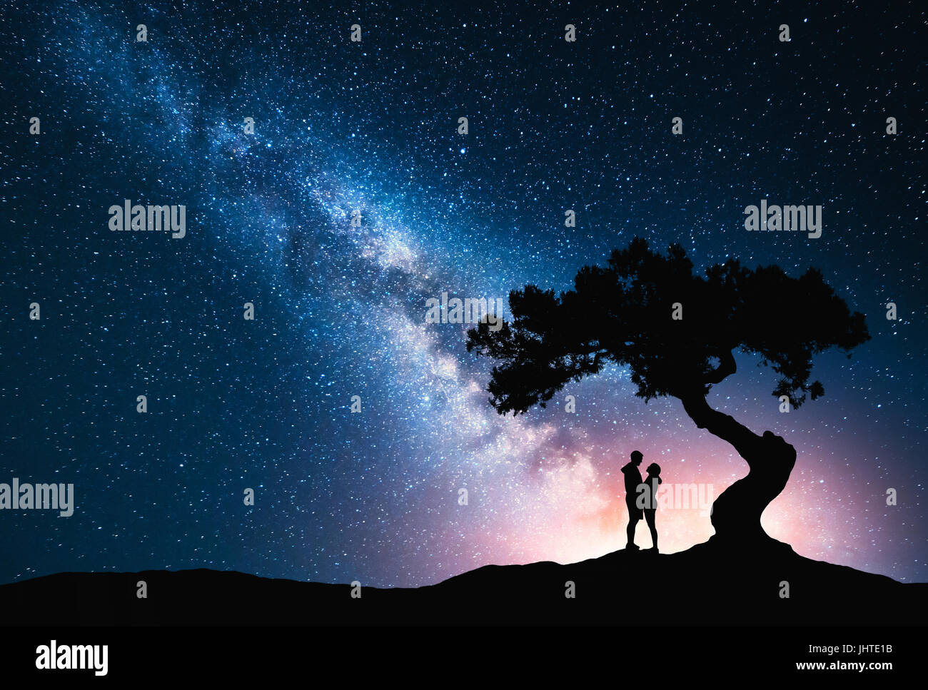 Milky Way with hugging couple under the tree on the hill. Landscape with night starry sky and silhouette of standing man and woman. Milky Way with you Stock Photo