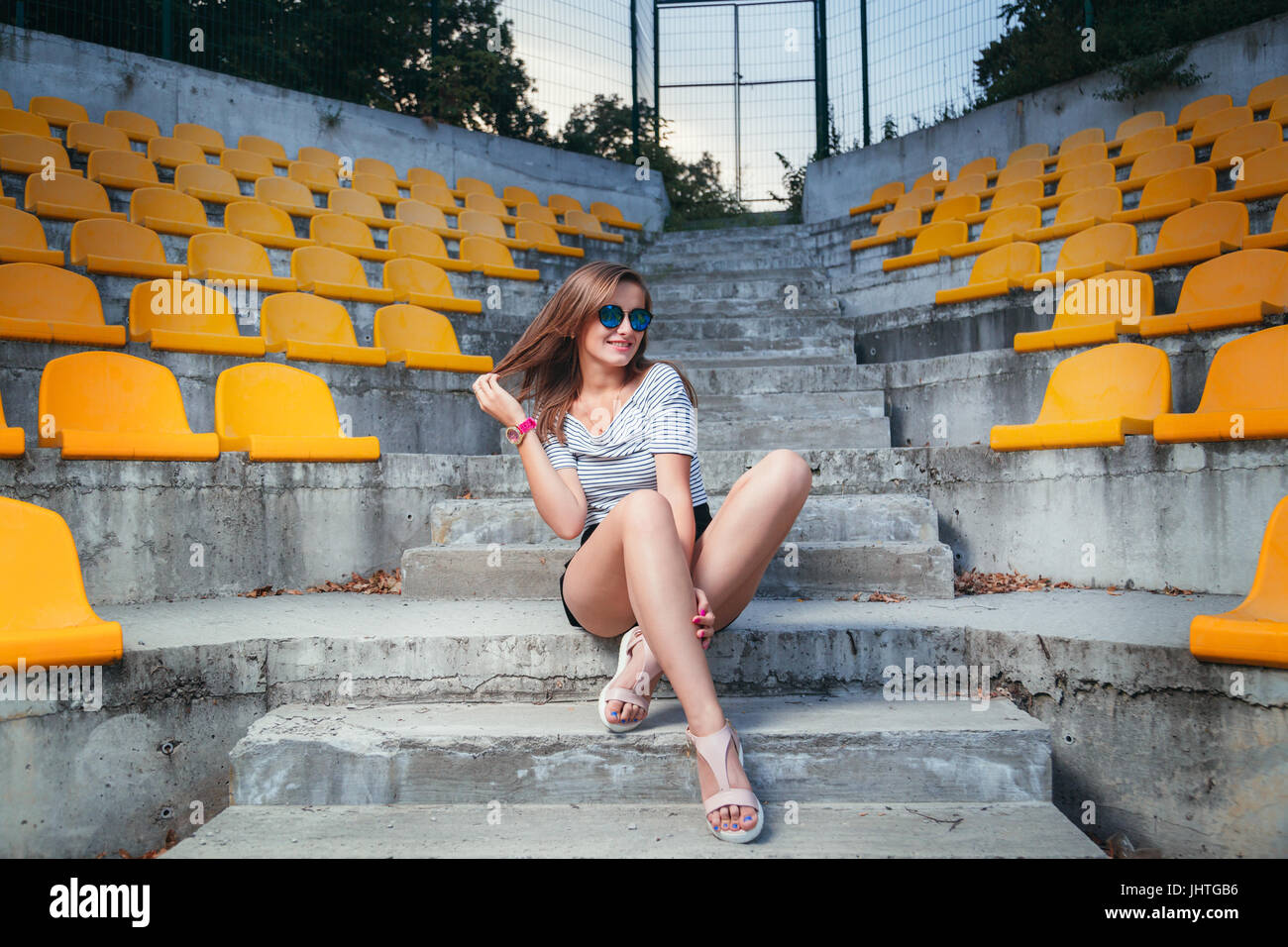 fashionable woman with round glasses sitting on the steps of the stadium outdoor Stock Photo