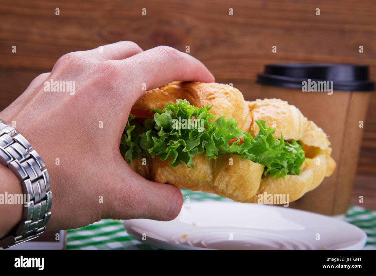 Croissant sandwich in hand. On the table coffee. Business lunch concept. Stock Photo