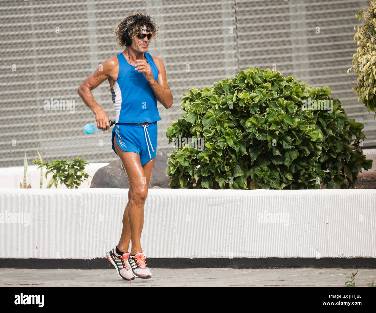Male jogger wearing headphones and sunglasses in city jogging through city streets. Stock Photo