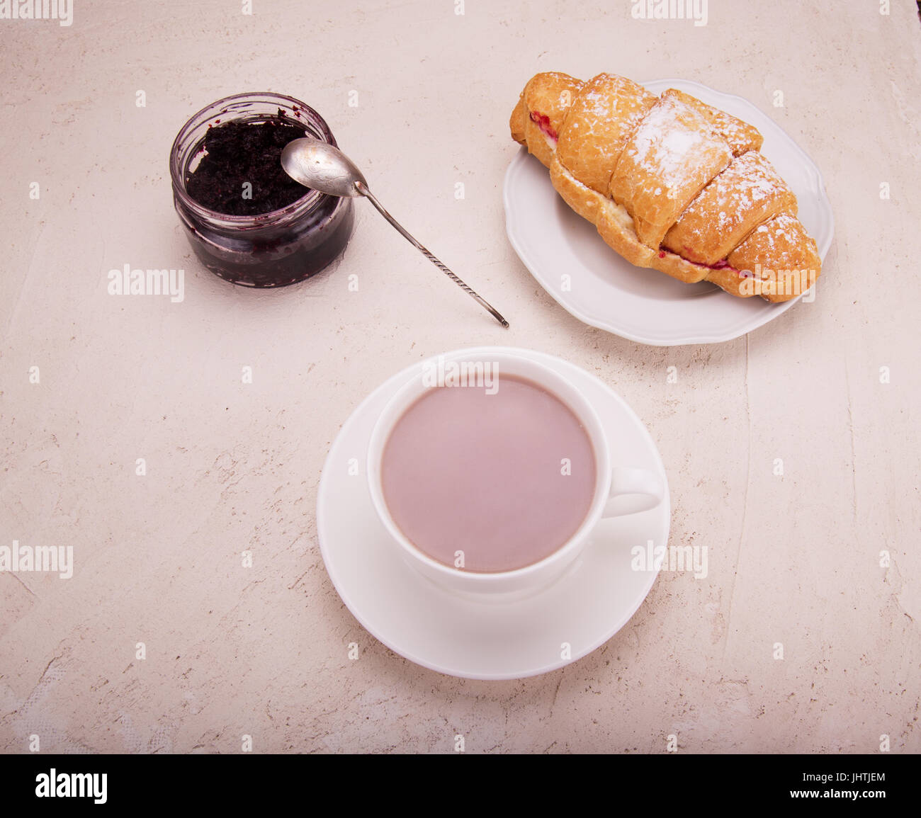 Croissant with raspberry jam, on the table a mobile phone and cocoa in a mug. The concept of business breakfast. Stock Photo