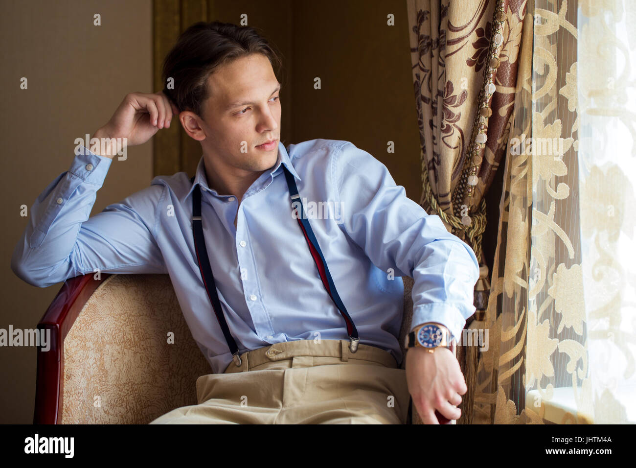 The groom is sitting in the armchair, looking out of the window, waiting. In the room. Stock Photo