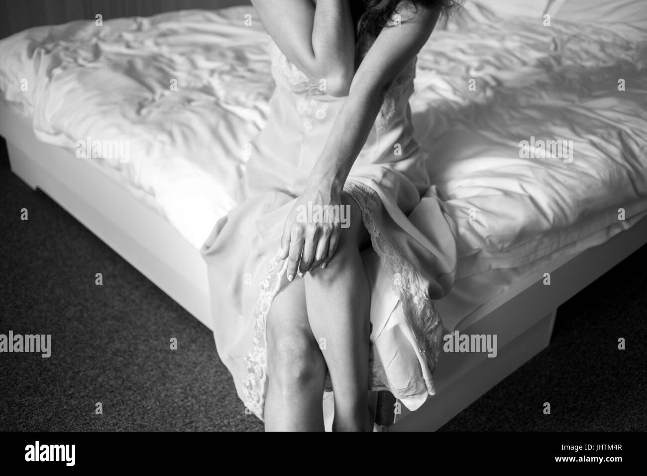 Beautiful cheerful pensive happy woman in nightie sitting on the bed. Cling to the knee. In the bedroom. Black and white. Stock Photo