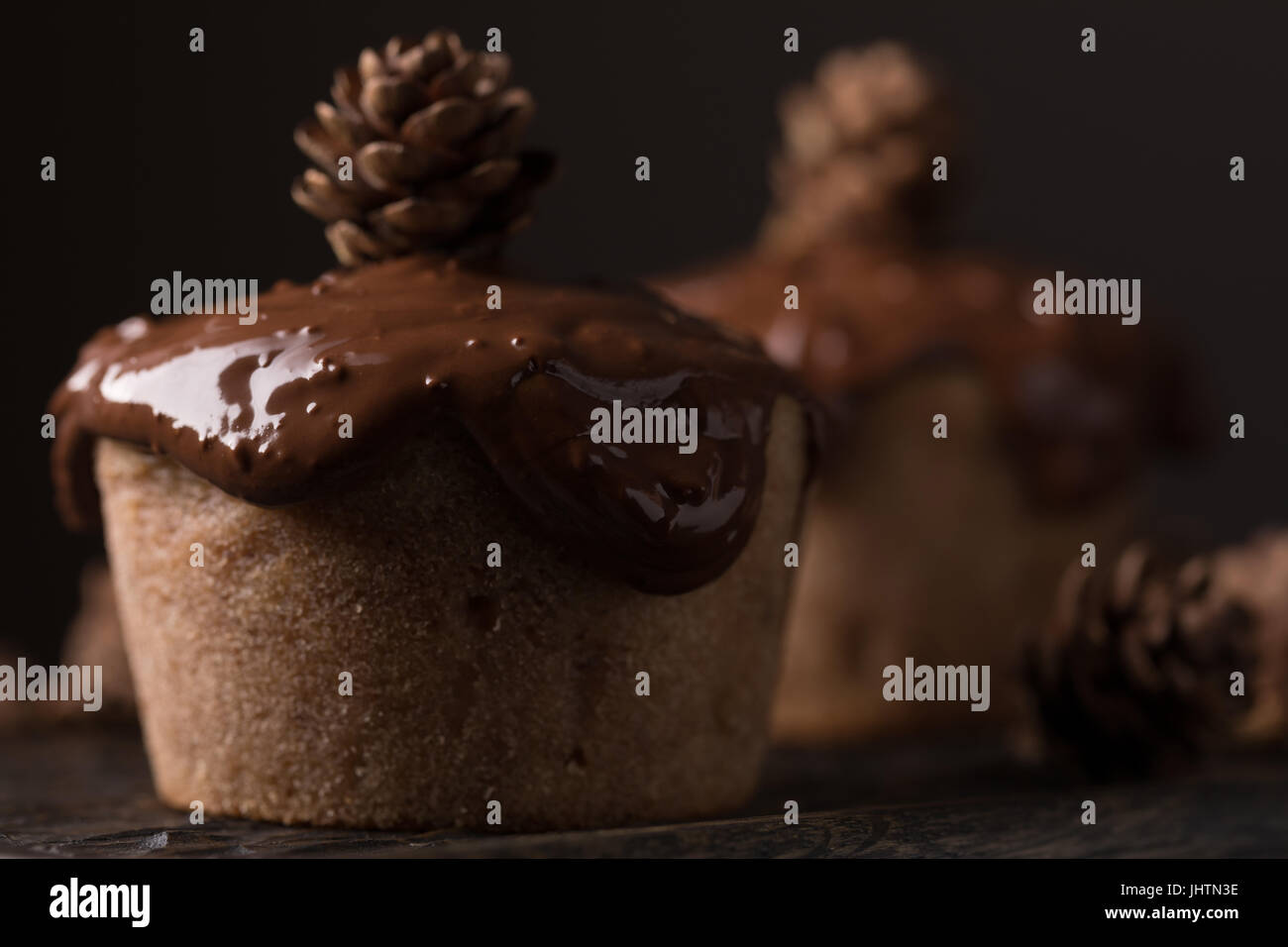 Chocolate muffins, decorated with a small cone on a dark wooden background. Low key. Cupcakes are poured with dark chocolate and cocoa powder. Cupcake Stock Photo