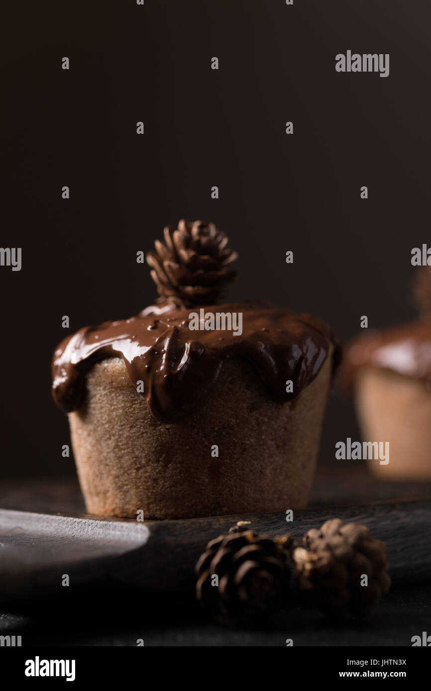 Chocolate muffins, decorated with a small cone on a dark wooden background. Low key. Cupcakes are poured with dark chocolate and cocoa powder. Cupcake Stock Photo