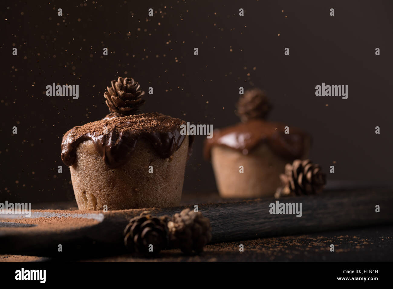 Chocolate muffins, decorated with a small cone on a dark wooden background. Low key. Cupcakes are poured with dark chocolate and cocoa powder. Cupcake Stock Photo