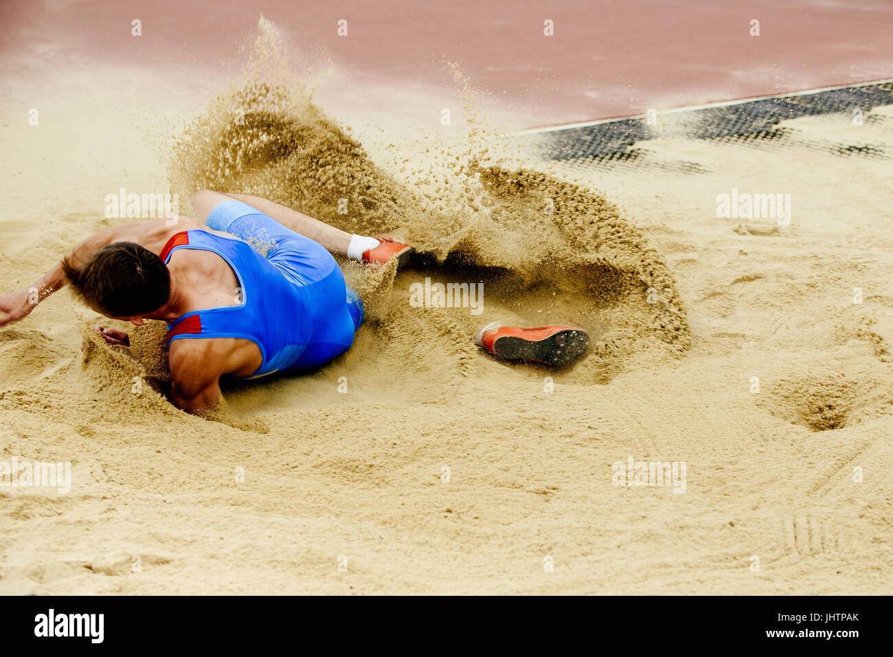 male athlete long jump landing sand spray Stock Photo