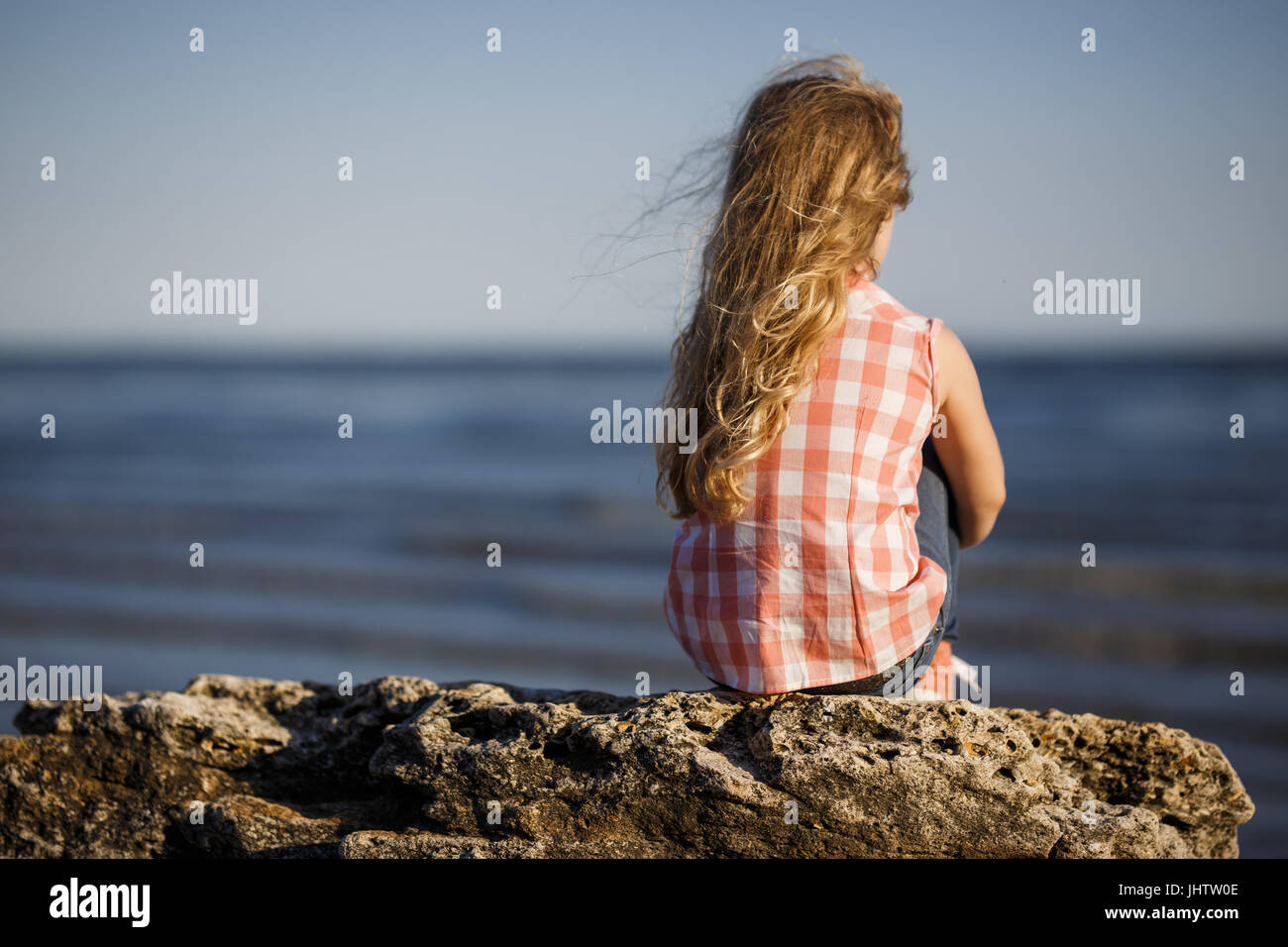 Little girl sits on a rocky shore and looks at the sea Stock Photo - Alamy