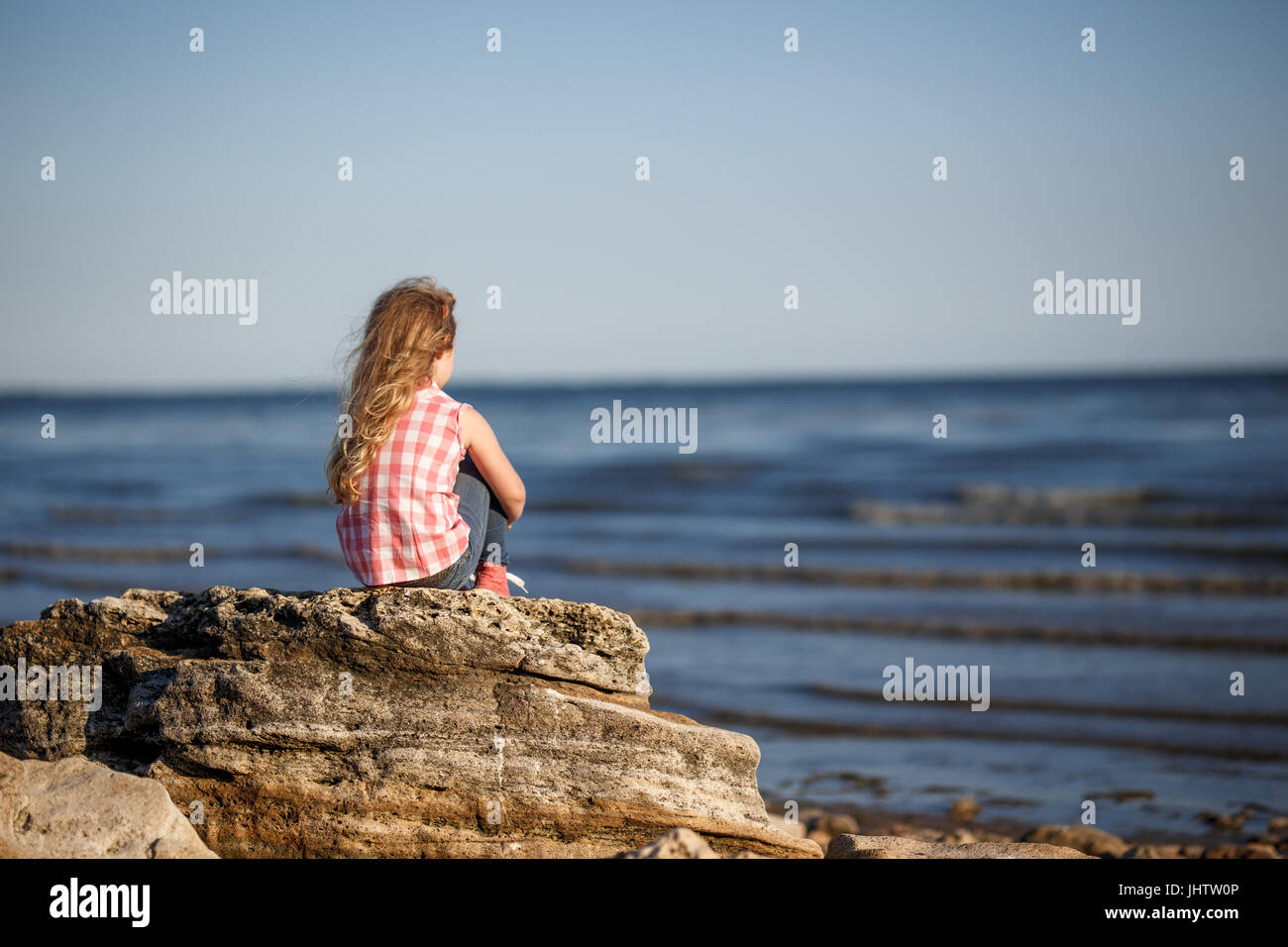 Little girl sits on a rocky shore and looks at the sea Stock Photo - Alamy