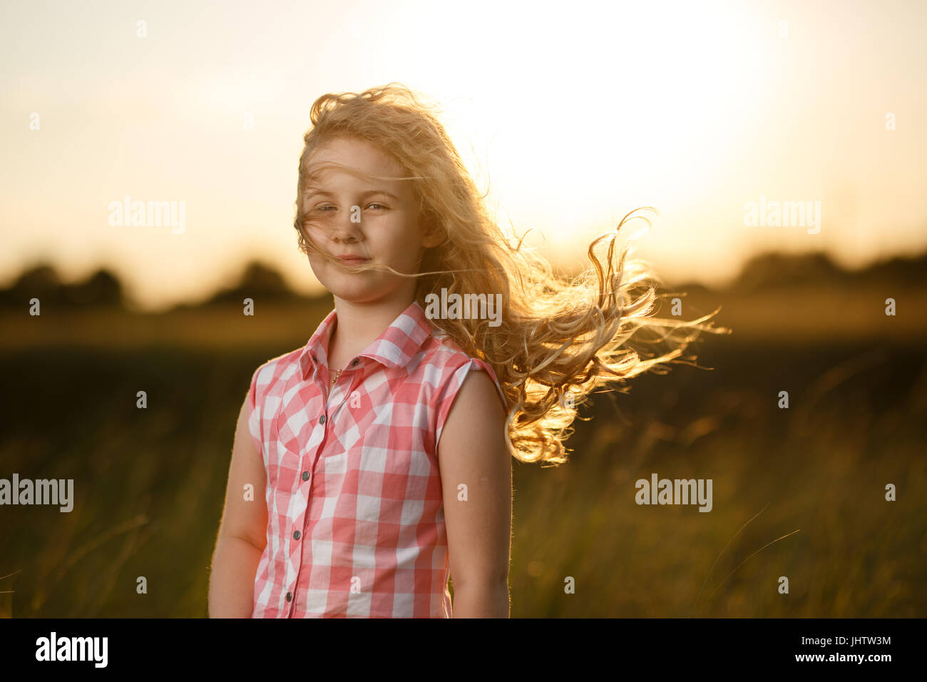 Little blonde child girl standing in summer field at sunset. Stock Photo