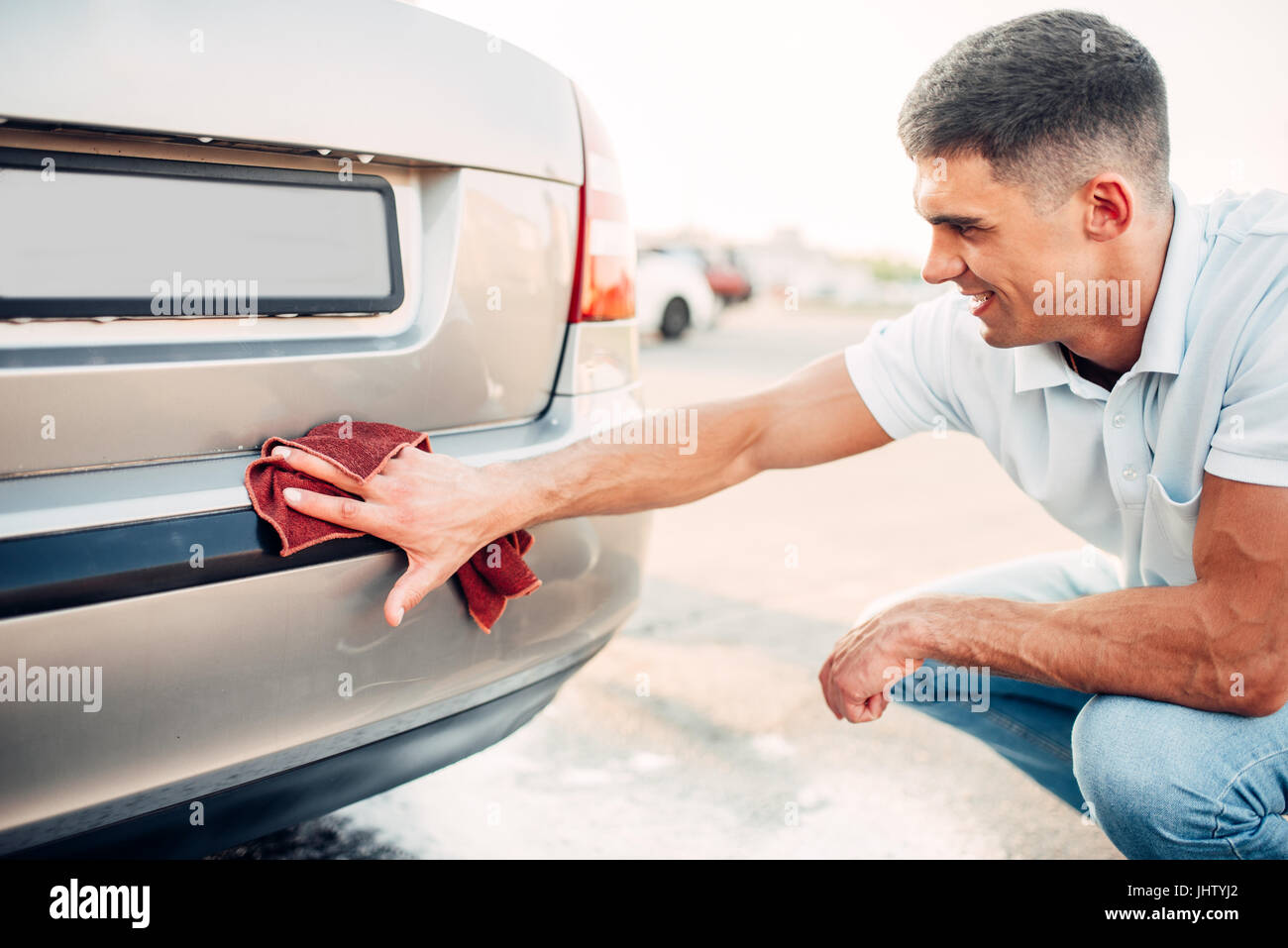 Car exterior polishing on carwash station. Man rubbing vehicle bumper