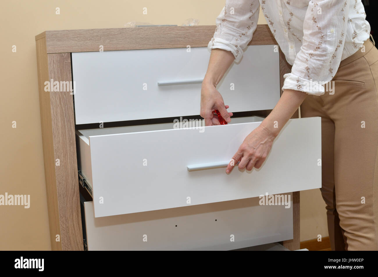 Woman Fixing A Pull On A Drawer Of A Cabinet With A Screwdriver
