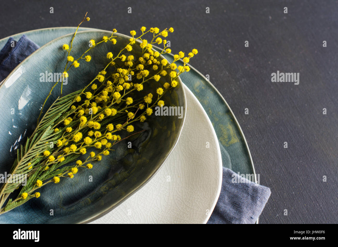 Festive table setting for Easter dinner with bright easter eggs and mimosa flowers on rustic plate Stock Photo