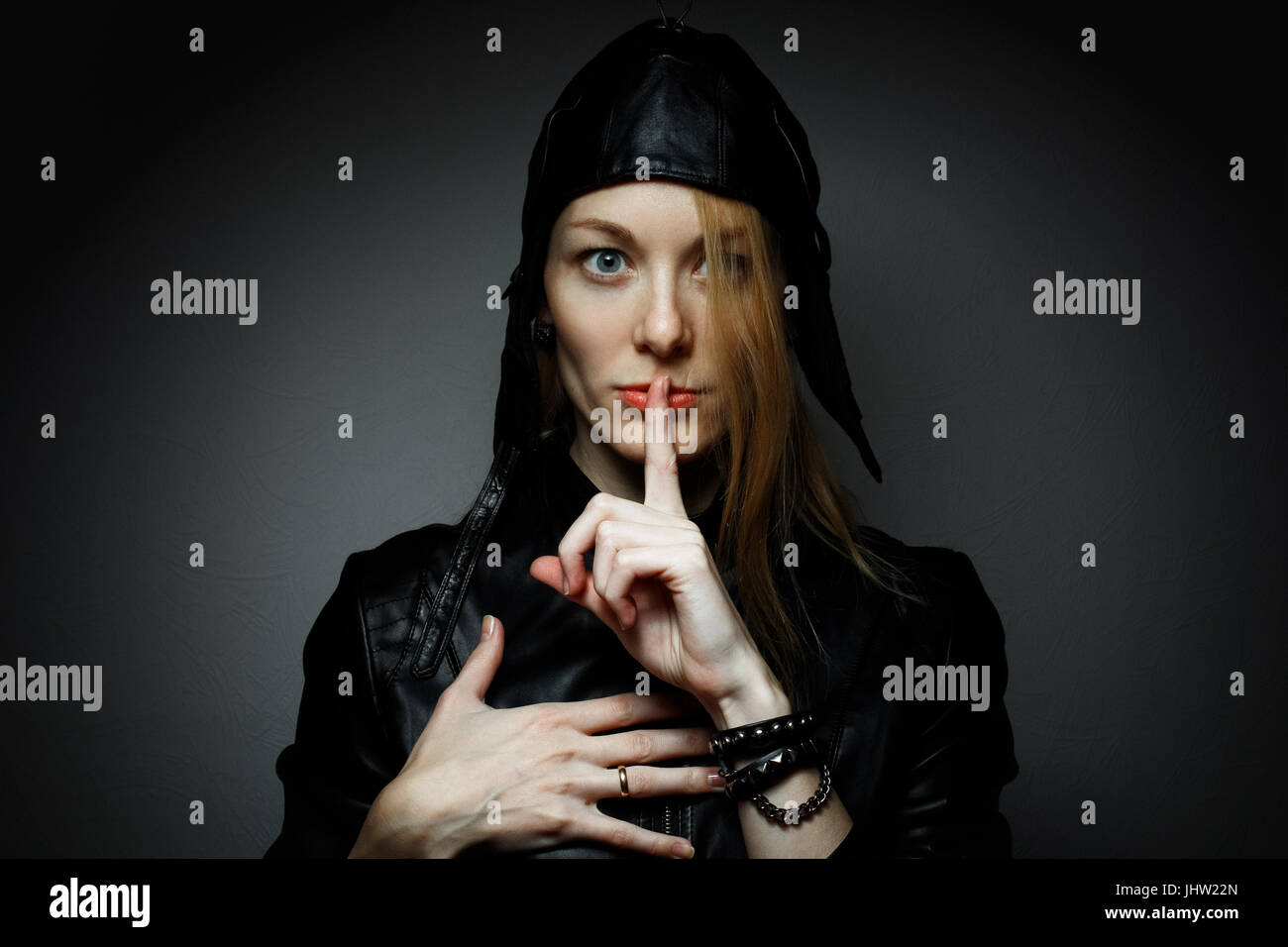 Young woman with red hairs gesturing for being quiet, shows silence sign in dark background Stock Photo