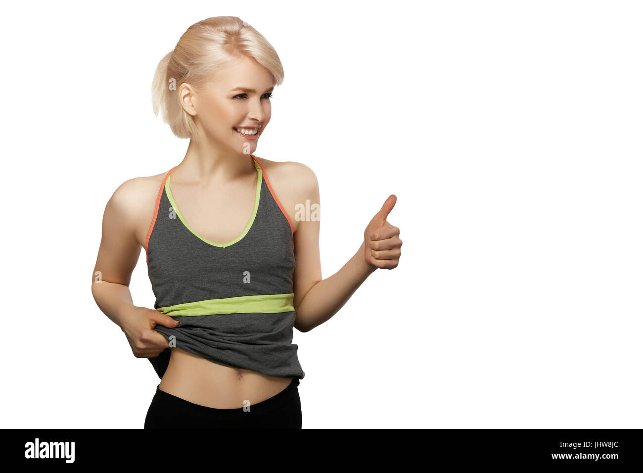 Slim girl in sportswear show her belly and thumb up isolated on white background Stock Photo