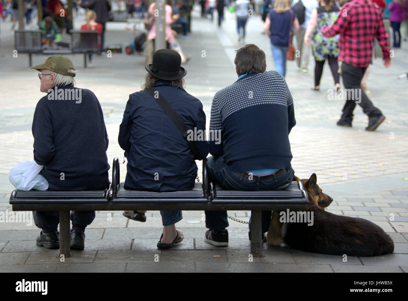 three male individuals and a dog sitting on a bench on sauchiehall street Glasgow Stock Photo